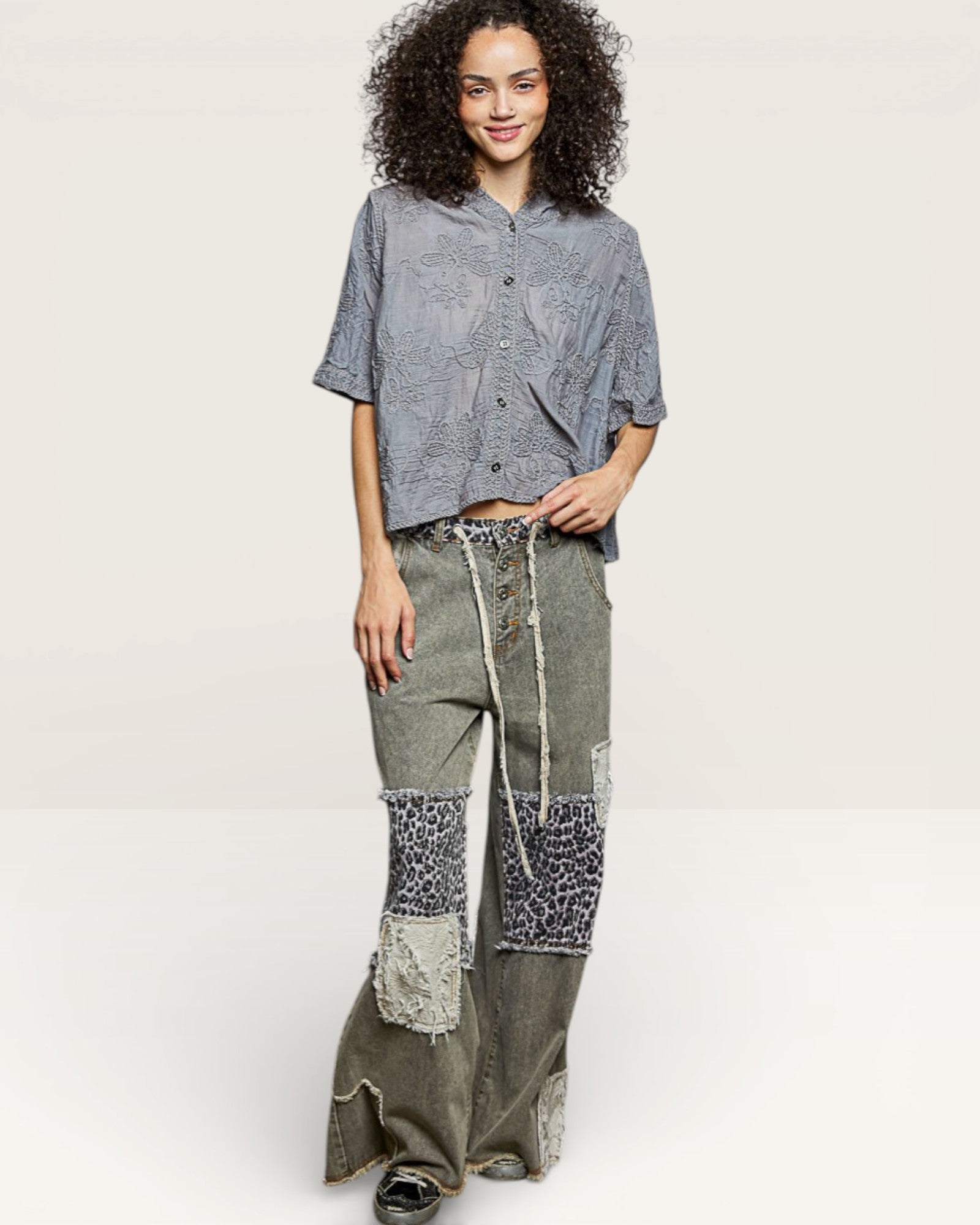 Woman wearing a gray patterned top and patchwork pants on a white background