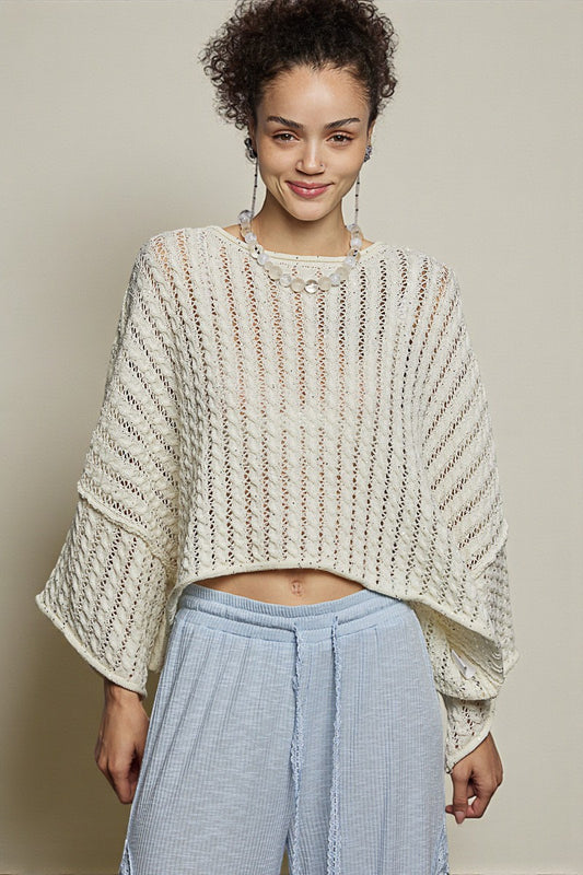 Woman wearing a textured beige sweater and light blue pants against a neutral background