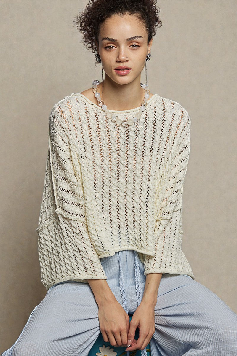 Woman wearing a textured beige sweater and light blue pants against a neutral background