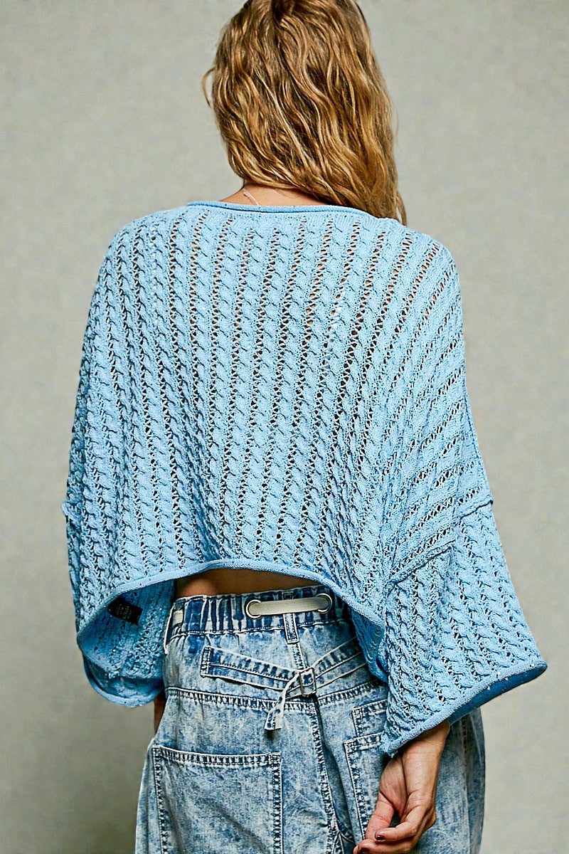Person wearing a light blue knitted sweater and jeans against a neutral background
