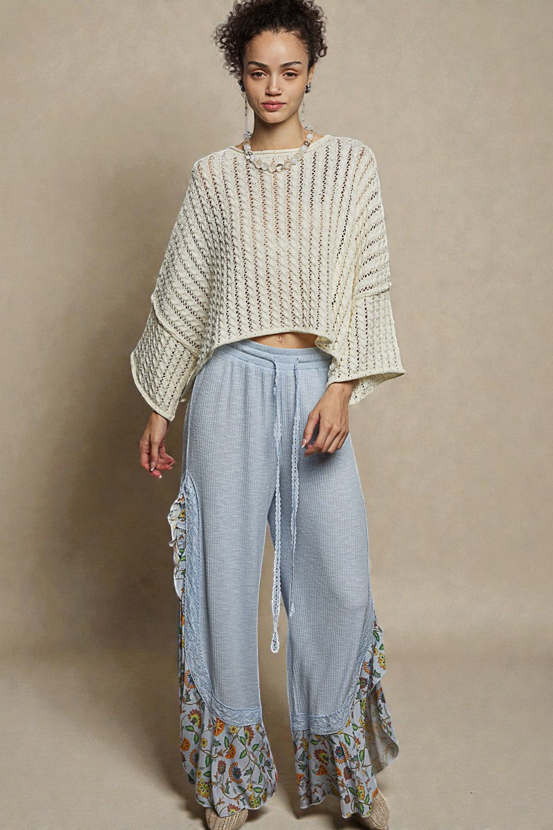 Woman wearing a textured sweater and light blue pants with floral details on a beige background