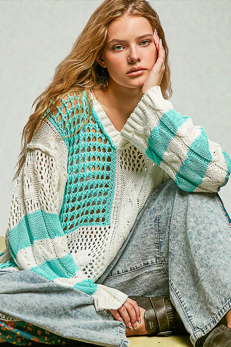 Woman wearing a colorful knitted cardigan and jeans sitting on the floor.