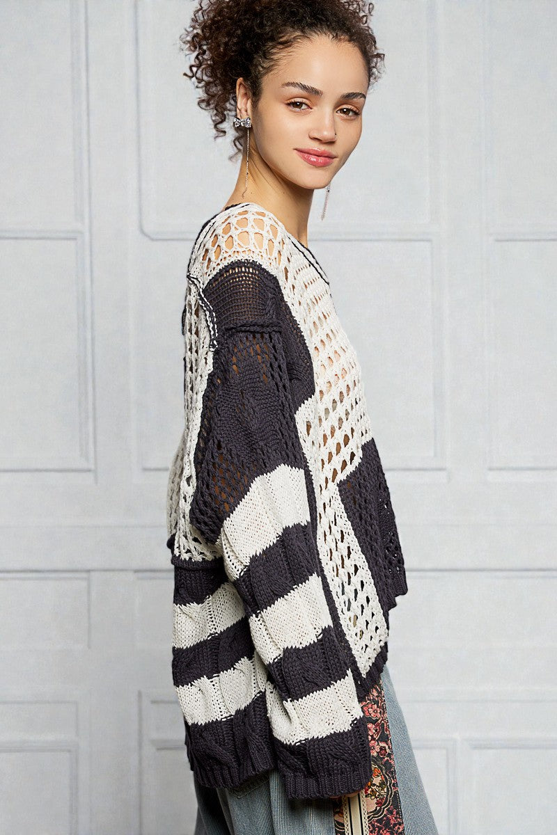 Woman wearing a black and white striped crochet cardigan against a light gray wall.