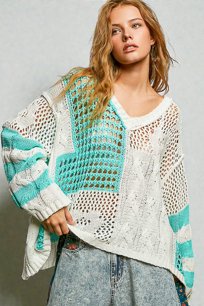 Woman wearing a crochet cardigan with teal and white patterns on a plain background