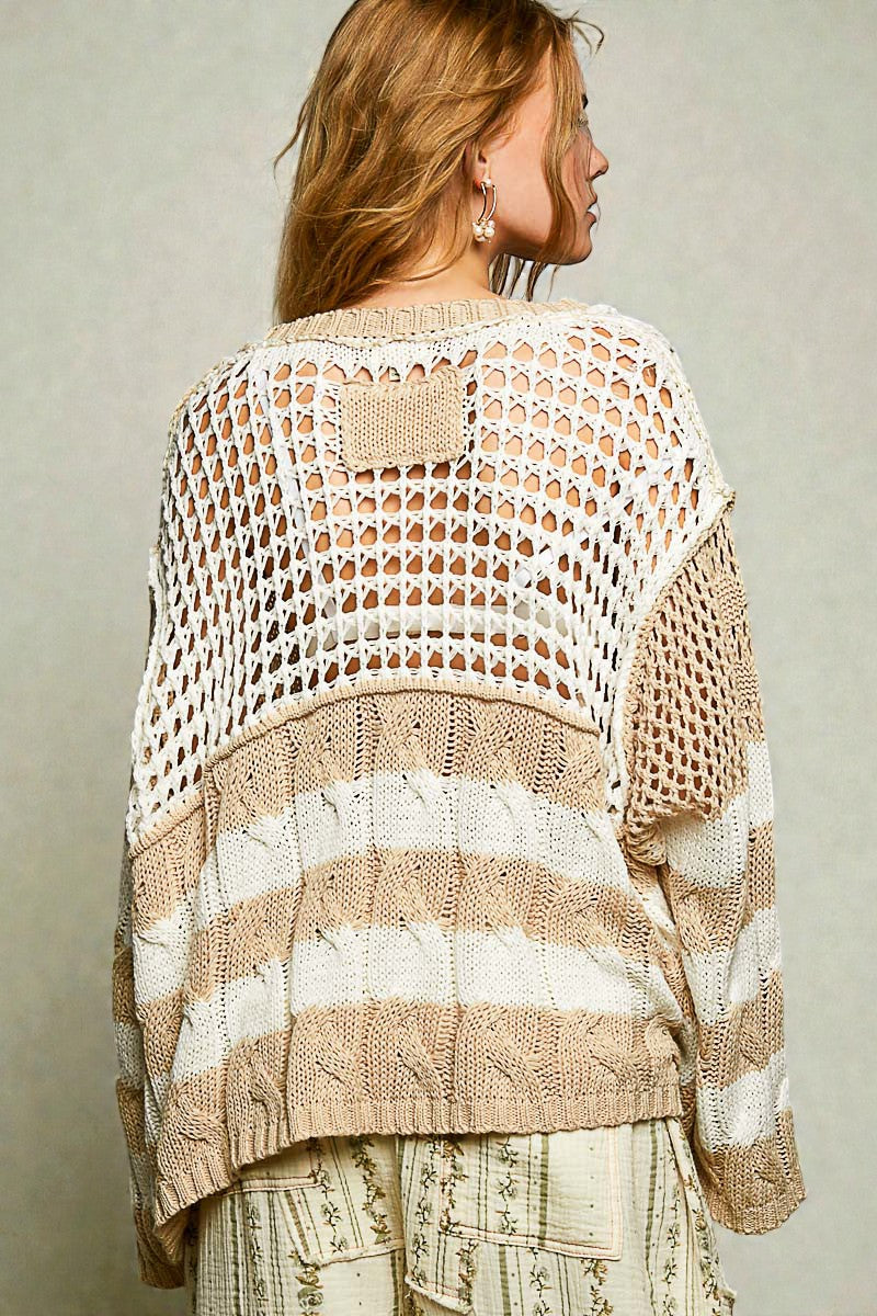Woman wearing a beige and white crochet poncho against a plain background