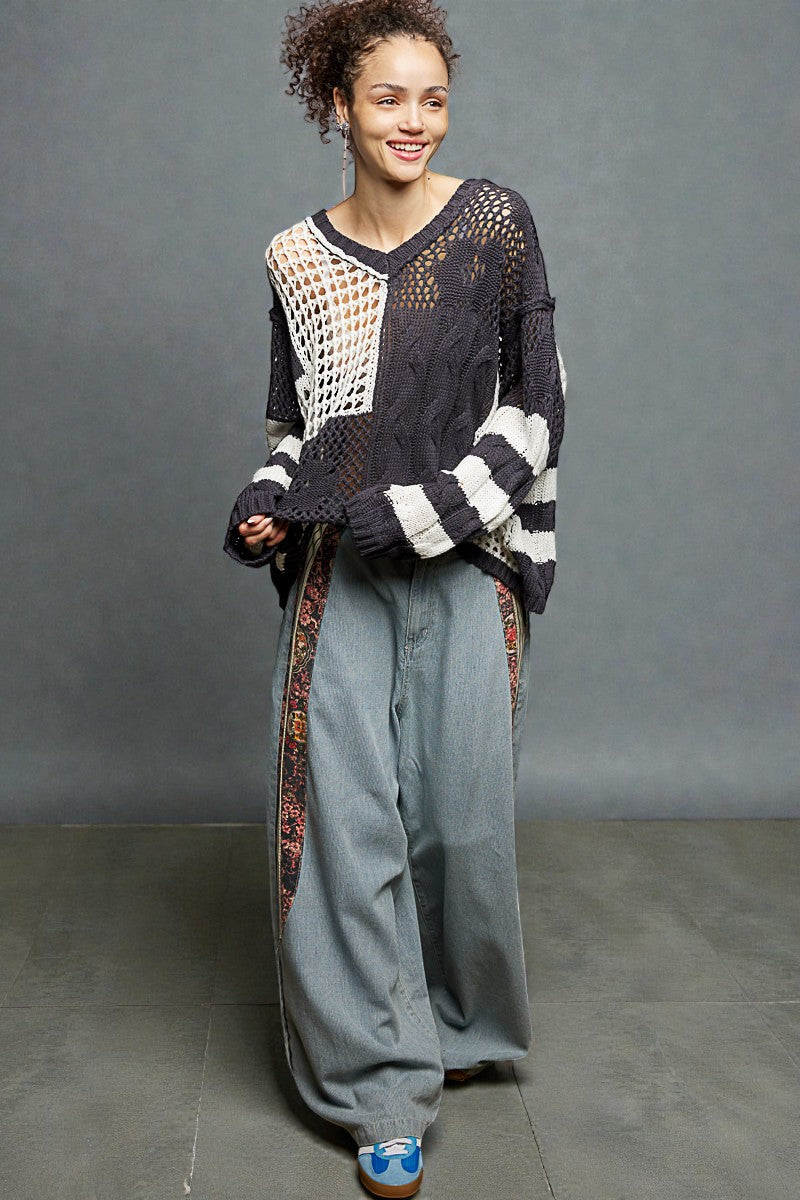 Woman wearing a black and white patterned sweater with gray pants against a gray background