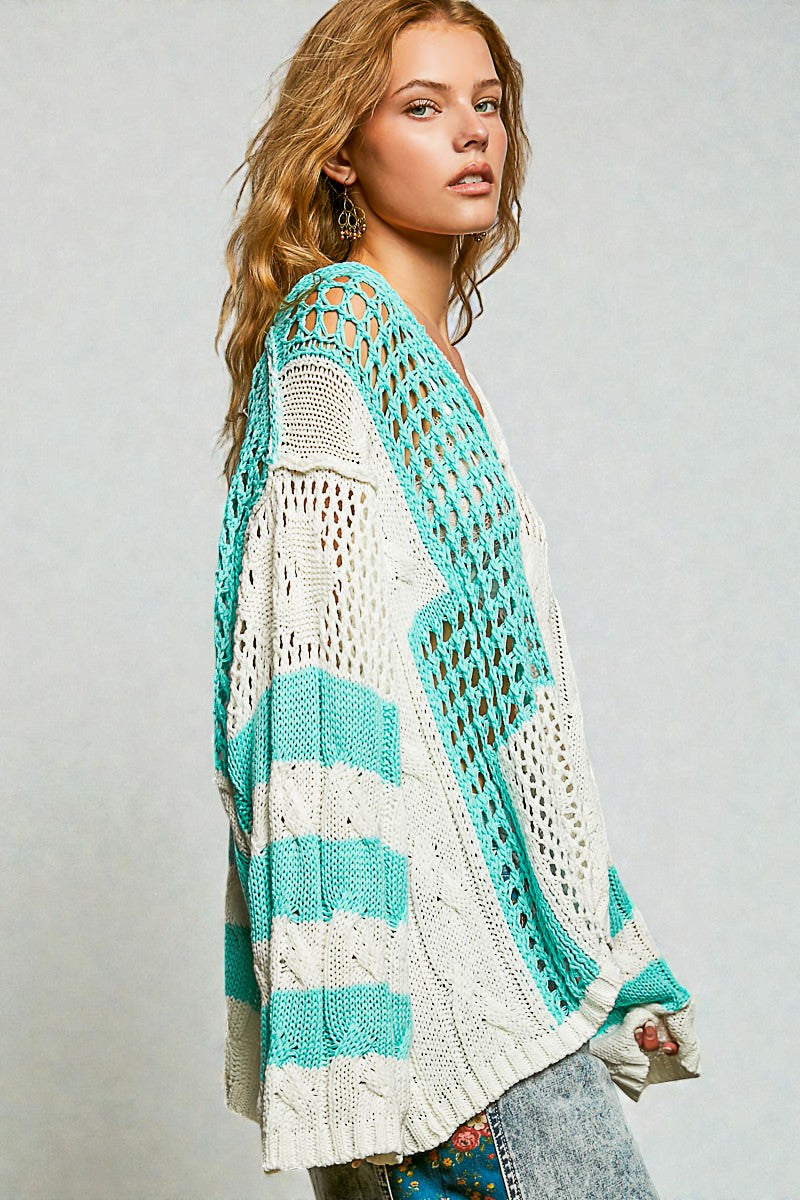 Woman wearing a teal and white crocheted cardigan on a plain background