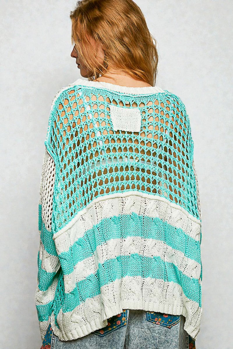 Woman wearing a turquoise and white crochet poncho against a plain background