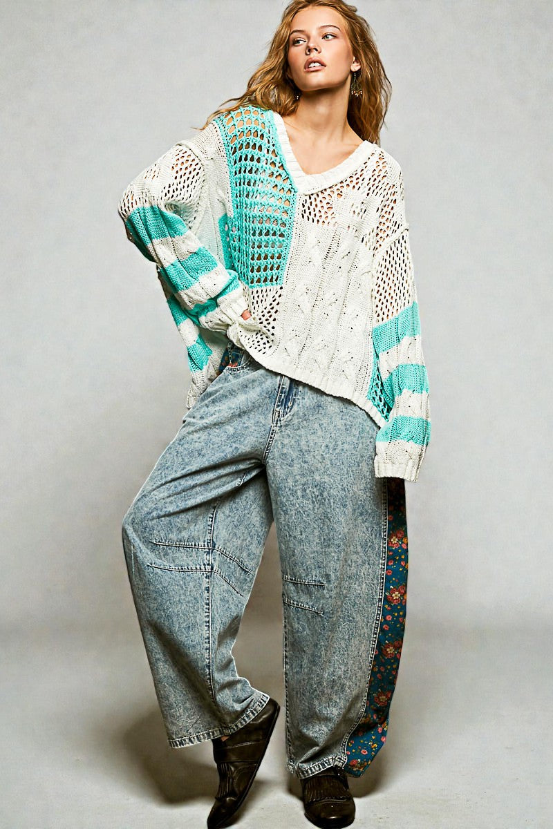 Woman wearing a crochet cardigan with teal and white pattern, paired with jeans and boots on a plain background