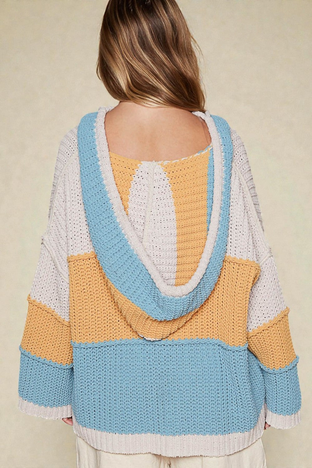 Person wearing a colorful striped sweater with a hood on a beige background