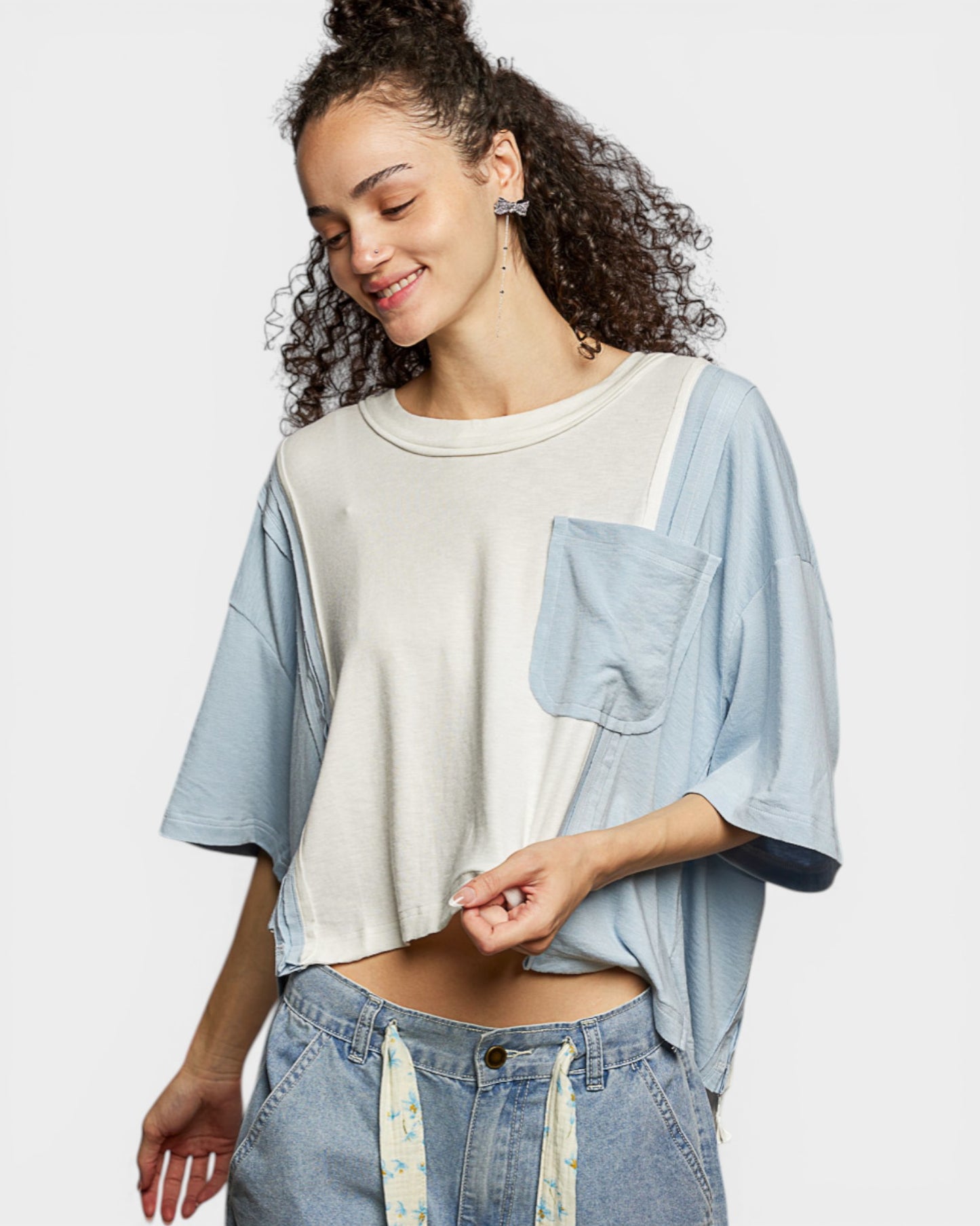 Woman wearing a light blue shirt over a beige top with denim pants on a white background