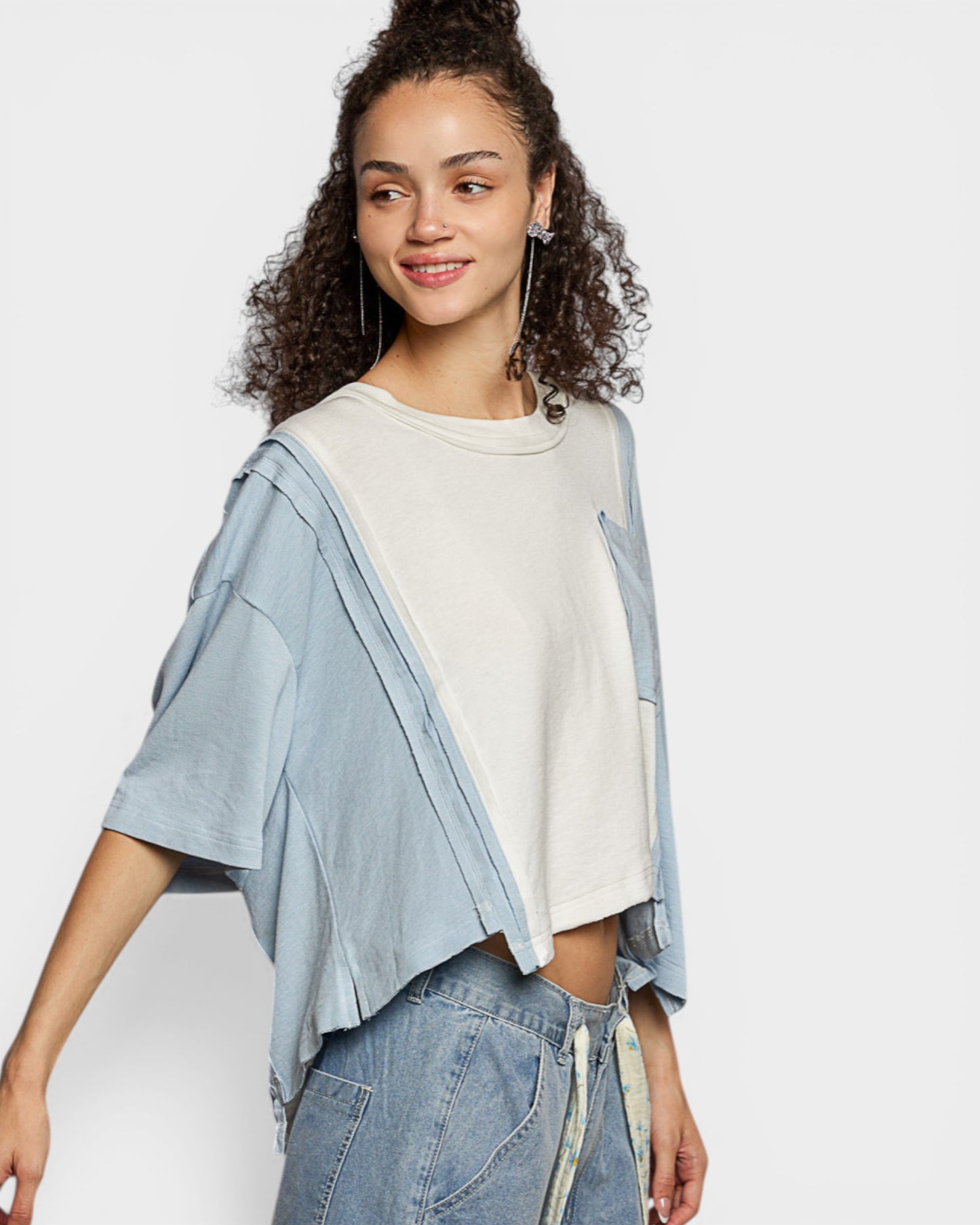 Woman wearing a light blue kimono-style top over a white shirt with jeans on a plain background