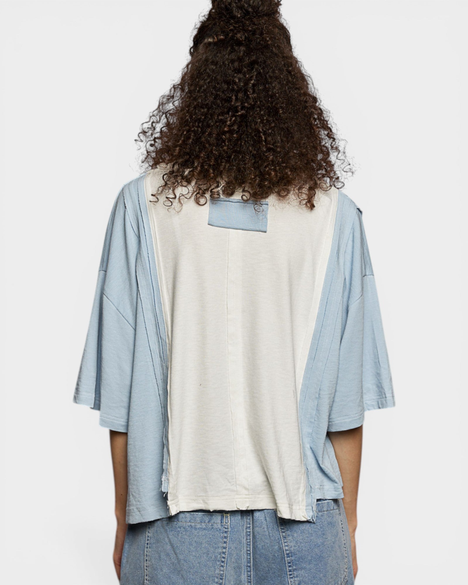 Person wearing a light blue shirt over a white t-shirt with a visible brand logo, standing against a plain background.