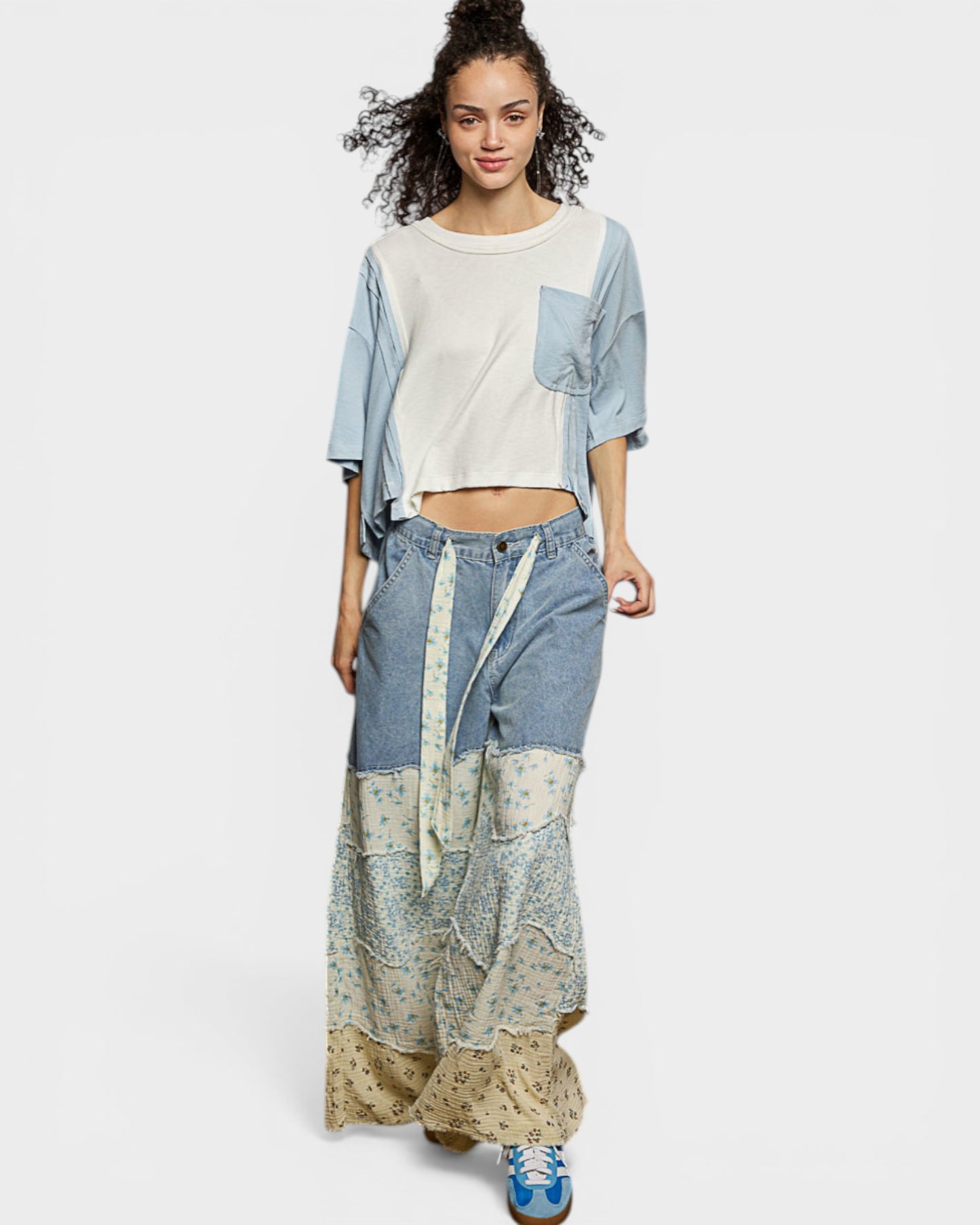 Woman wearing a patchwork outfit with a white top, denim jacket, and patterned pants on a white background