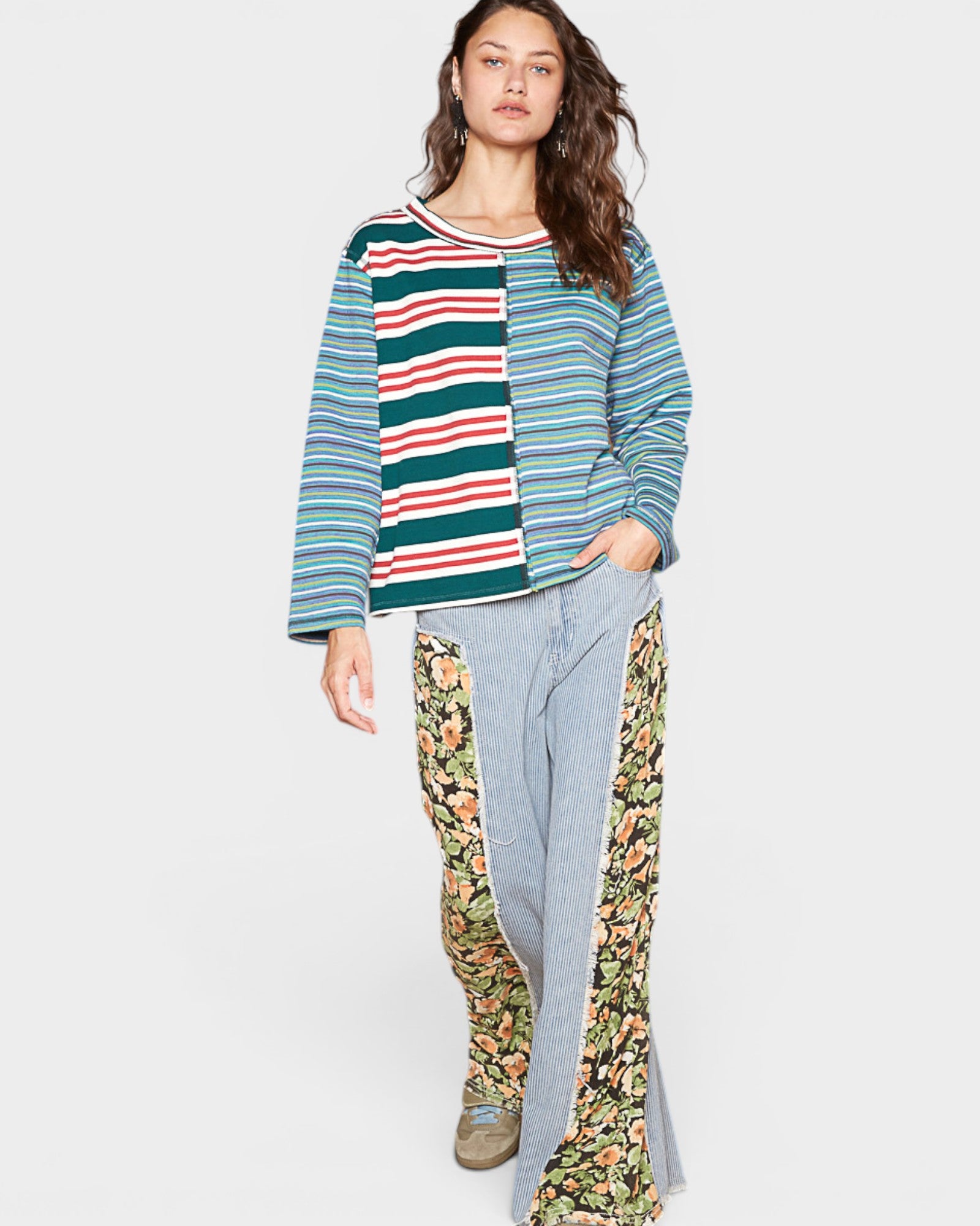Woman wearing a colorful striped sweater and floral pants on a white background