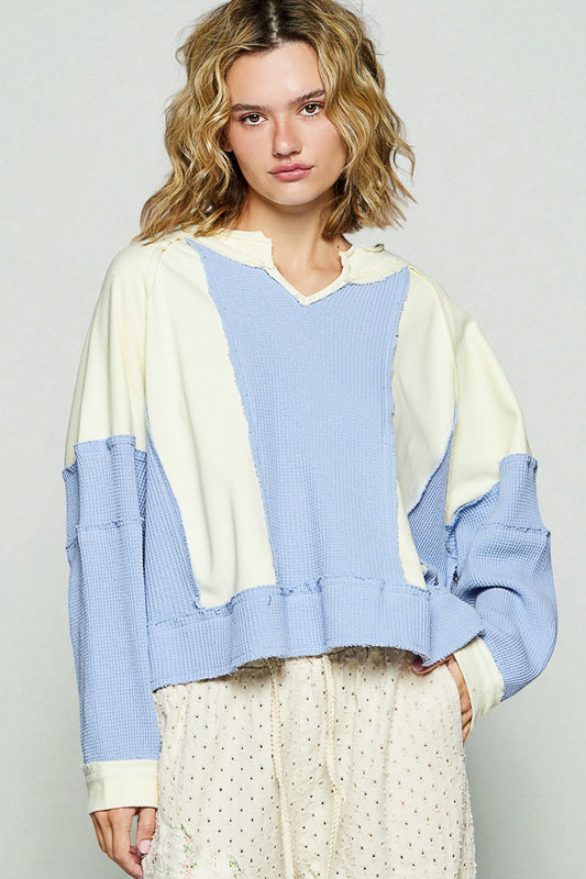 Woman wearing a color-blocked sweater with blue and beige tones on a plain background