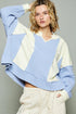 Woman wearing a blue and beige color-blocked sweater against a gray background