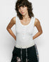 Woman wearing a white sleeveless top with colorful buttons and black pants with floral embroidery on a light gray background