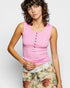 Woman wearing a pink sleeveless top with colorful buttons against a plain background