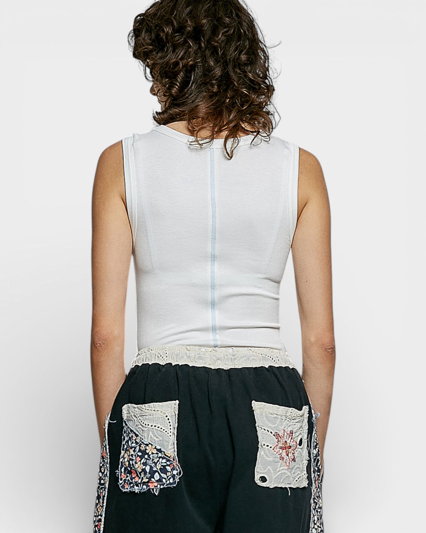 Person wearing a white sleeveless top and black pants with floral embroidery on a plain background