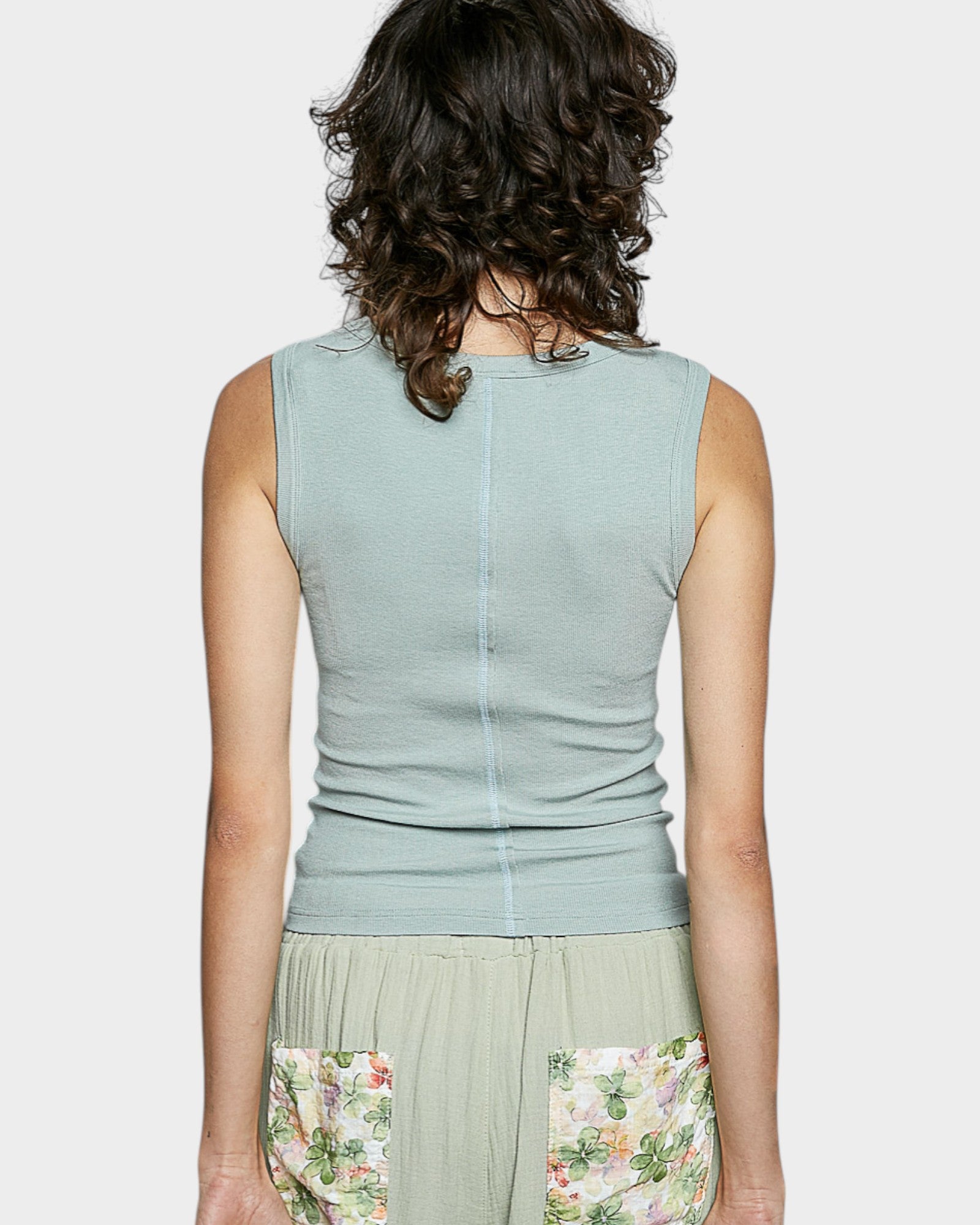 Woman wearing a light green sleeveless top with floral skirt on a white background