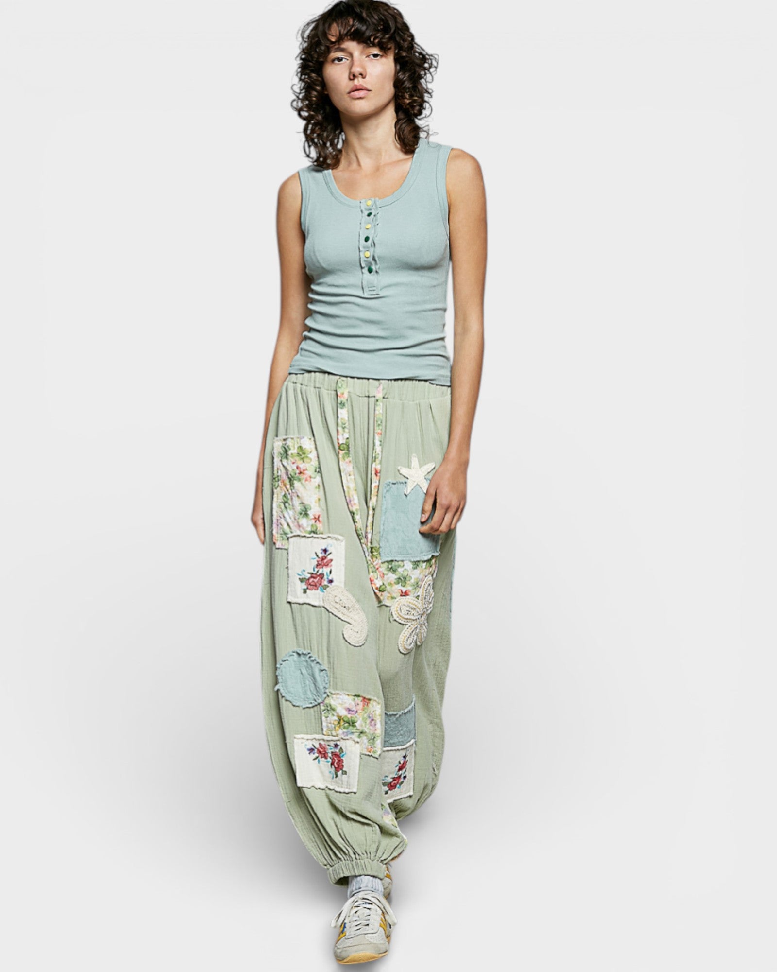 Woman wearing a sleeveless top and floral patch pants on a white background