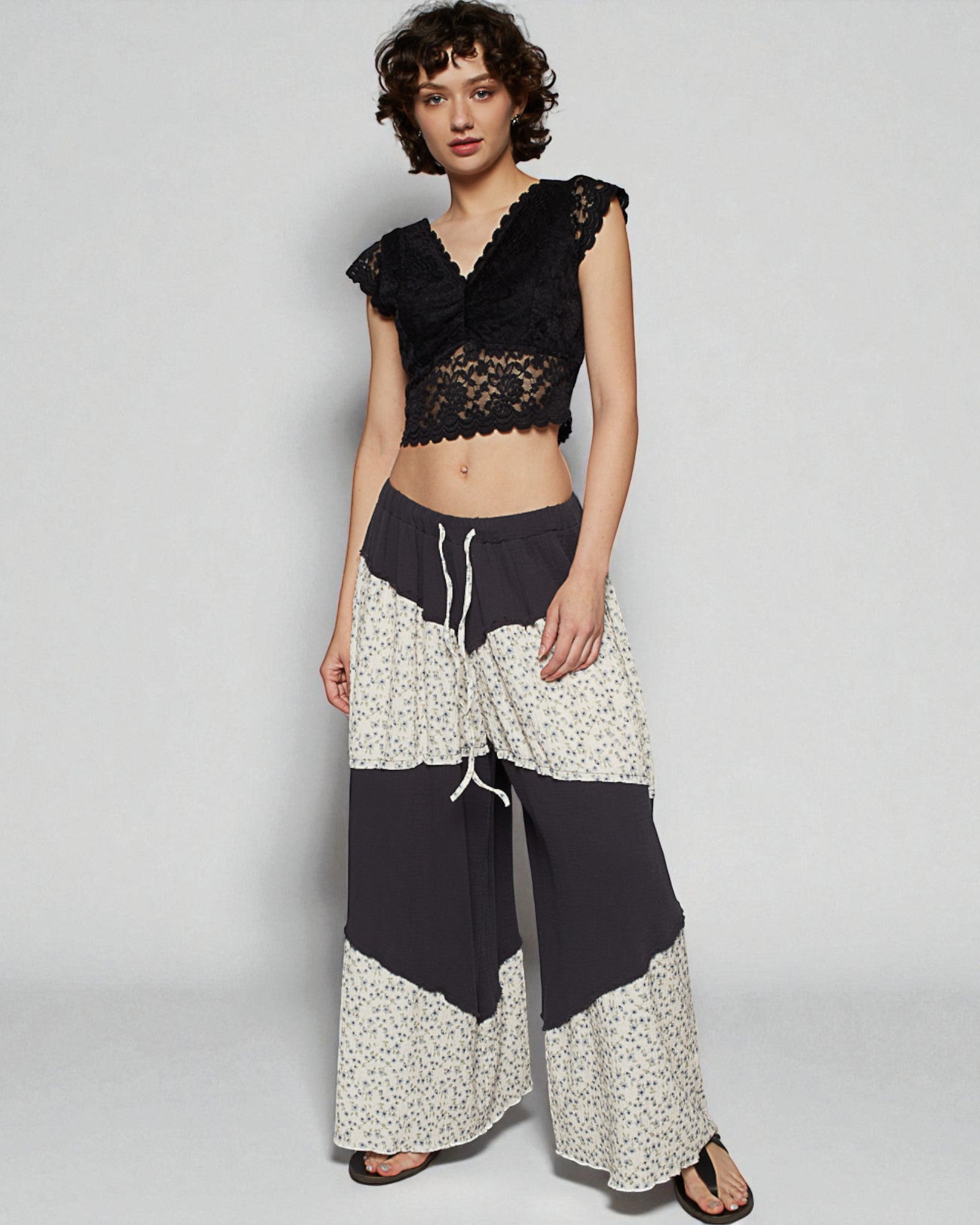 Woman wearing a black lace top and floral pants on a plain background