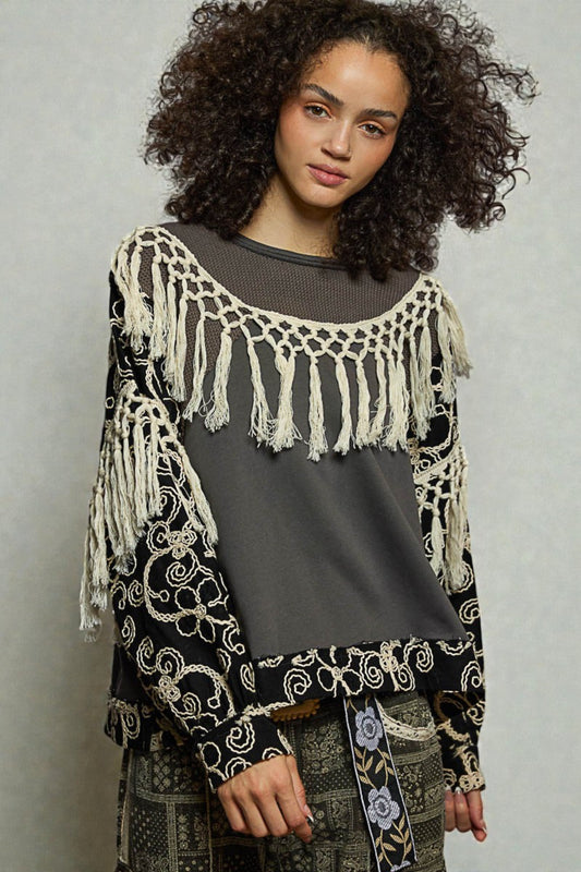 Woman wearing a black and white patterned top with fringe details on a gray background