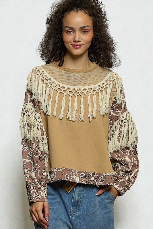 Woman wearing a beige top with lace details and patterned sleeves against a white background