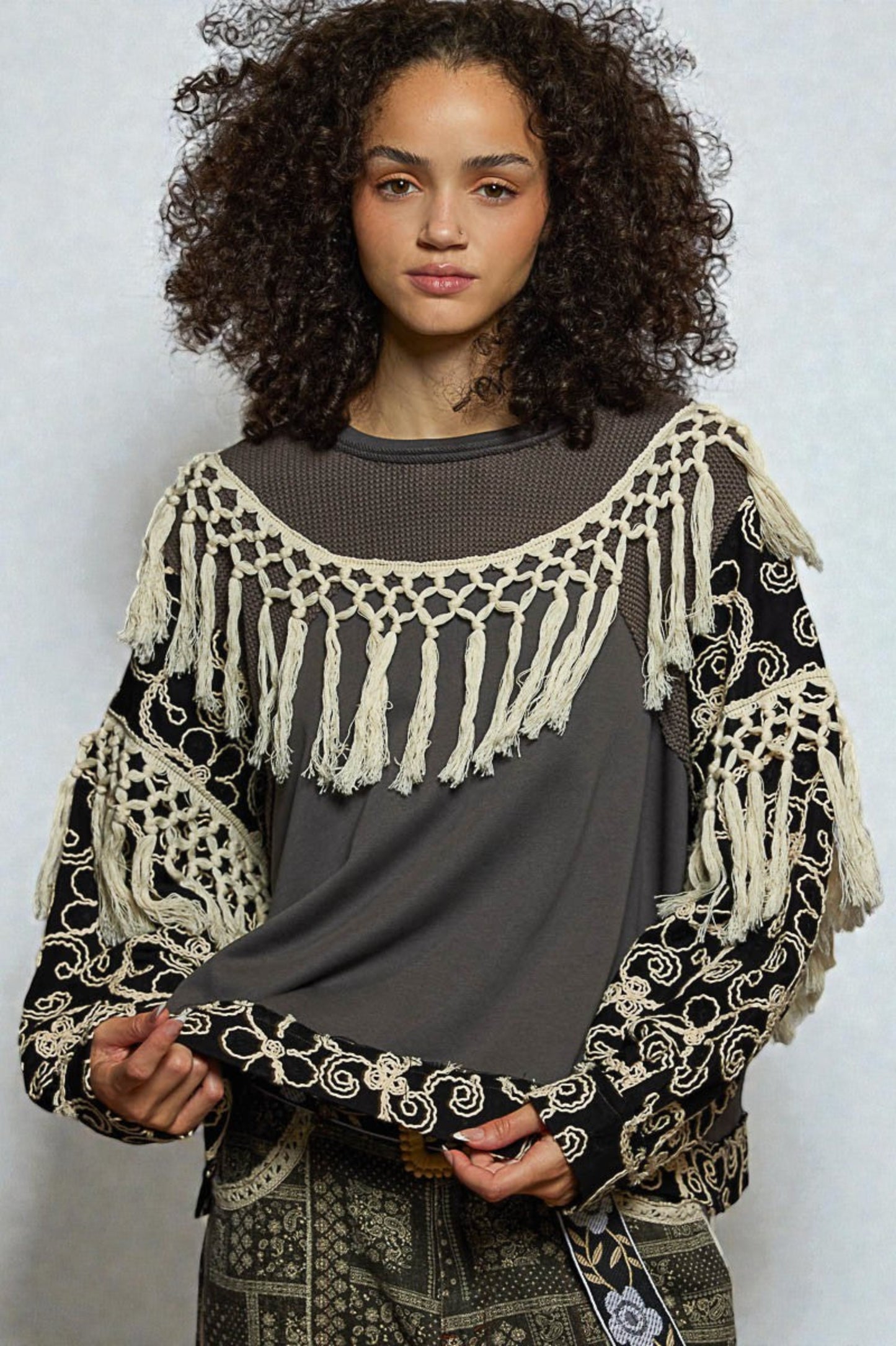 Woman wearing a black and beige patterned shawl with fringe on a plain background