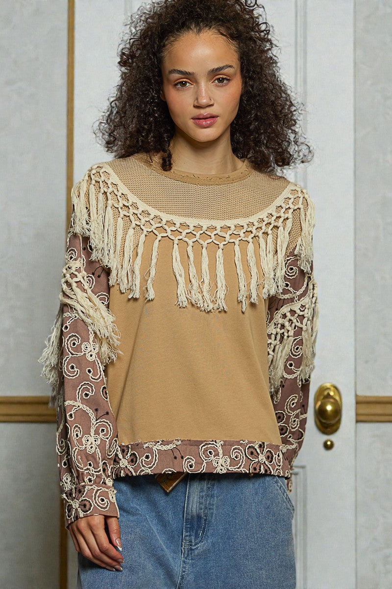 Woman wearing a beige top with lace details and patterned sleeves in front of a door.