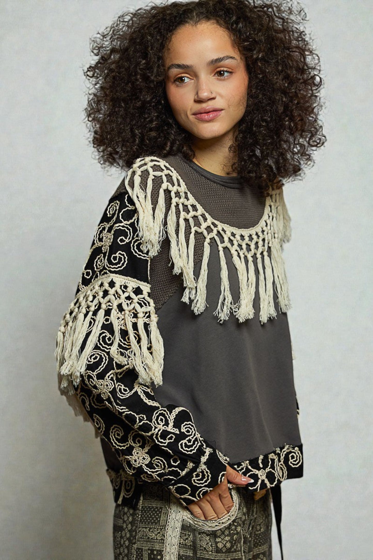 Woman wearing a black and white patterned top with fringes on a plain background