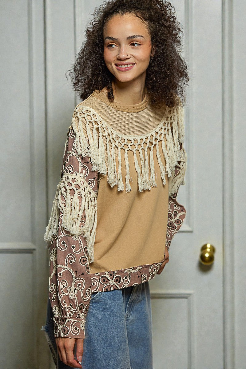 Woman wearing a patterned top with fringe details in front of a white door.