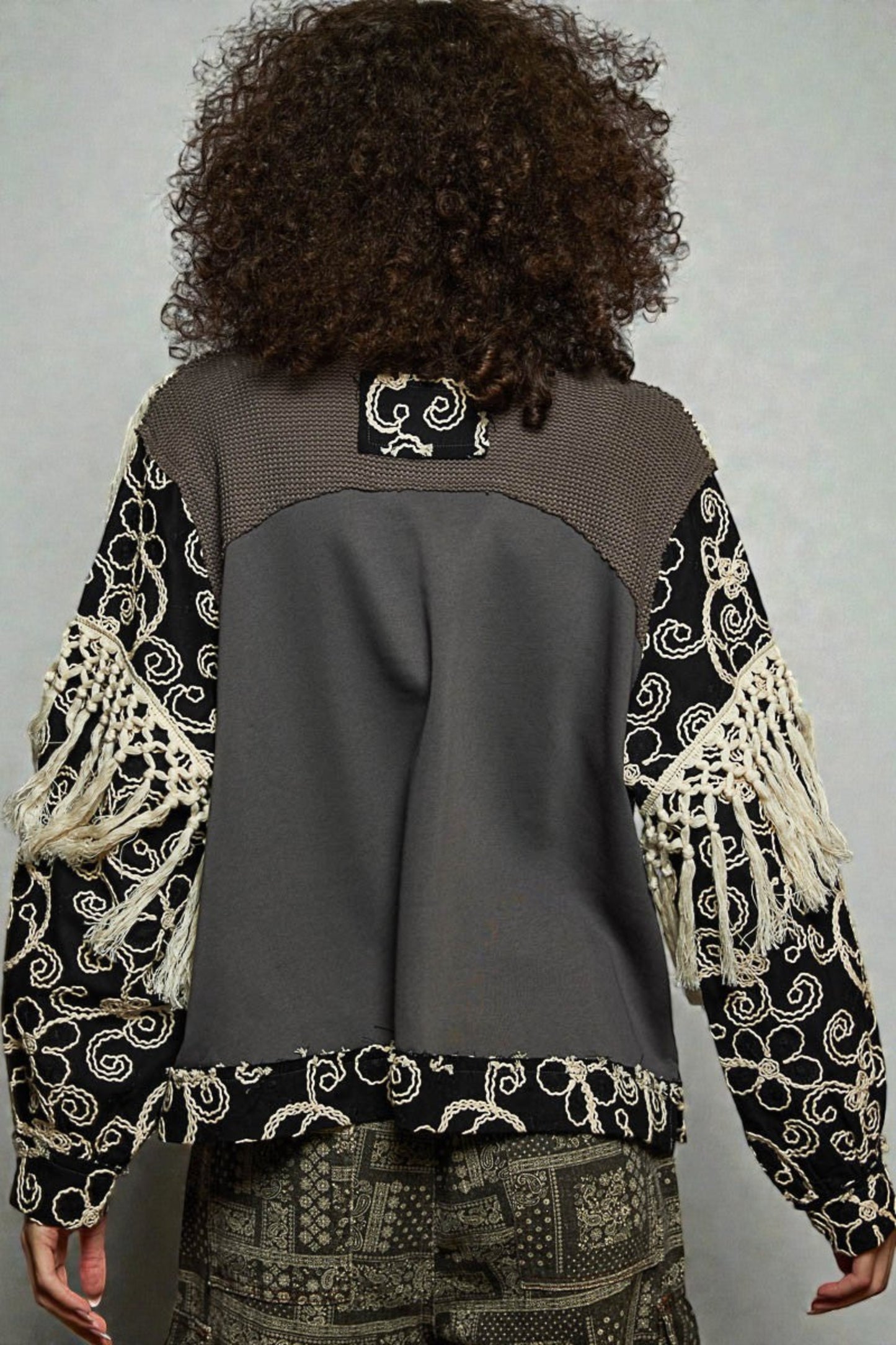 Person wearing a patterned jacket with a gray back, standing against a plain background