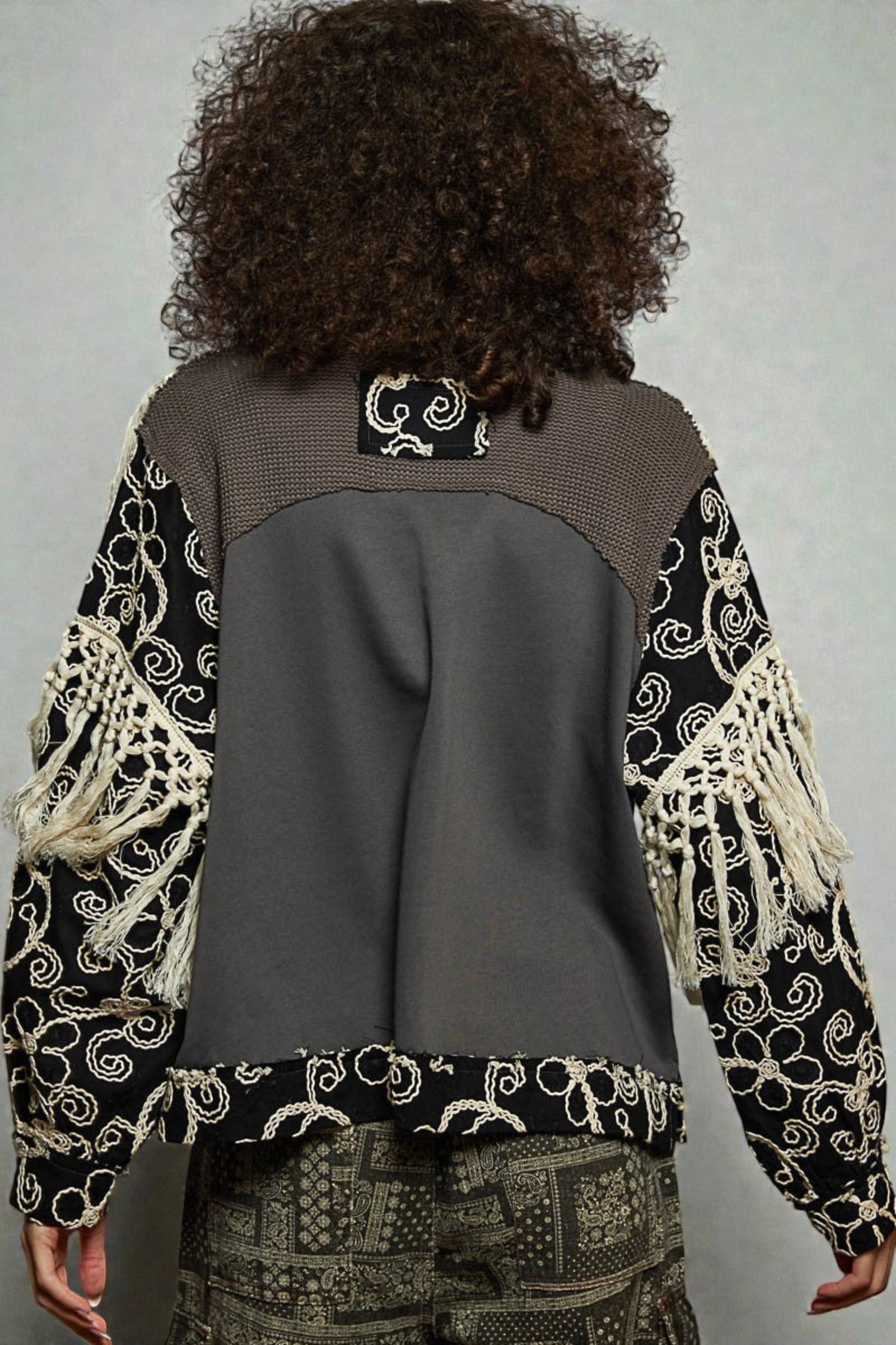 Person wearing a patterned jacket with a gray back, standing against a plain background