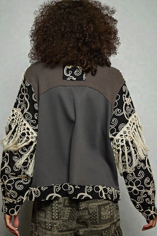 Person wearing a patterned jacket with a gray back, standing against a plain background