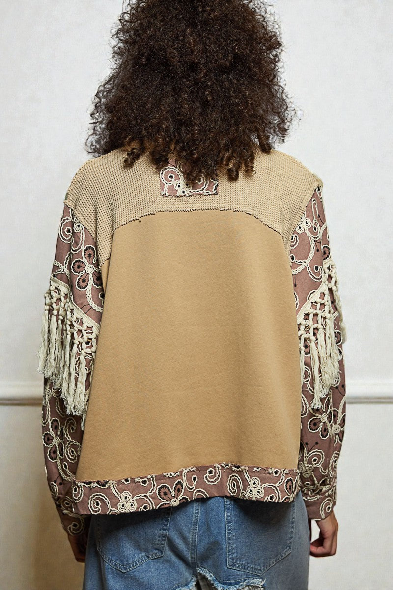 Person wearing a beige vest with patterned sleeves and back, standing against a plain background.