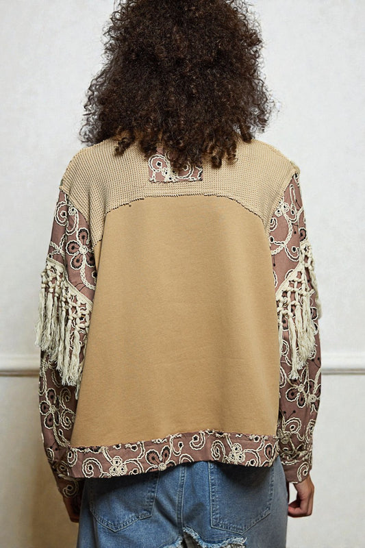 Person wearing a beige vest with patterned sleeves and back, standing against a plain background.