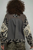 Person wearing a patterned jacket with a gray back, standing against a plain background