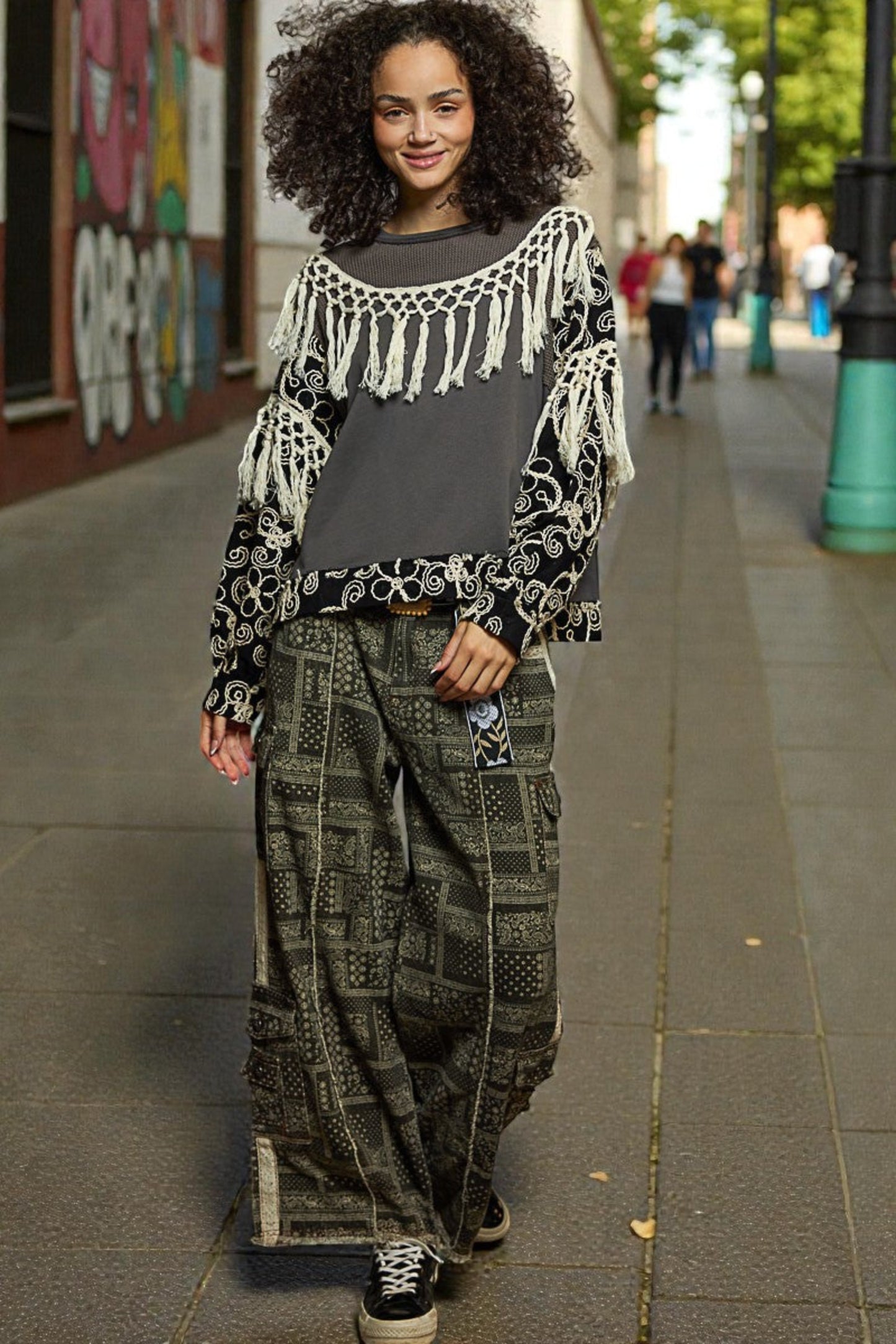 Woman wearing a stylish outfit with a patterned top and baggy pants on a city street.