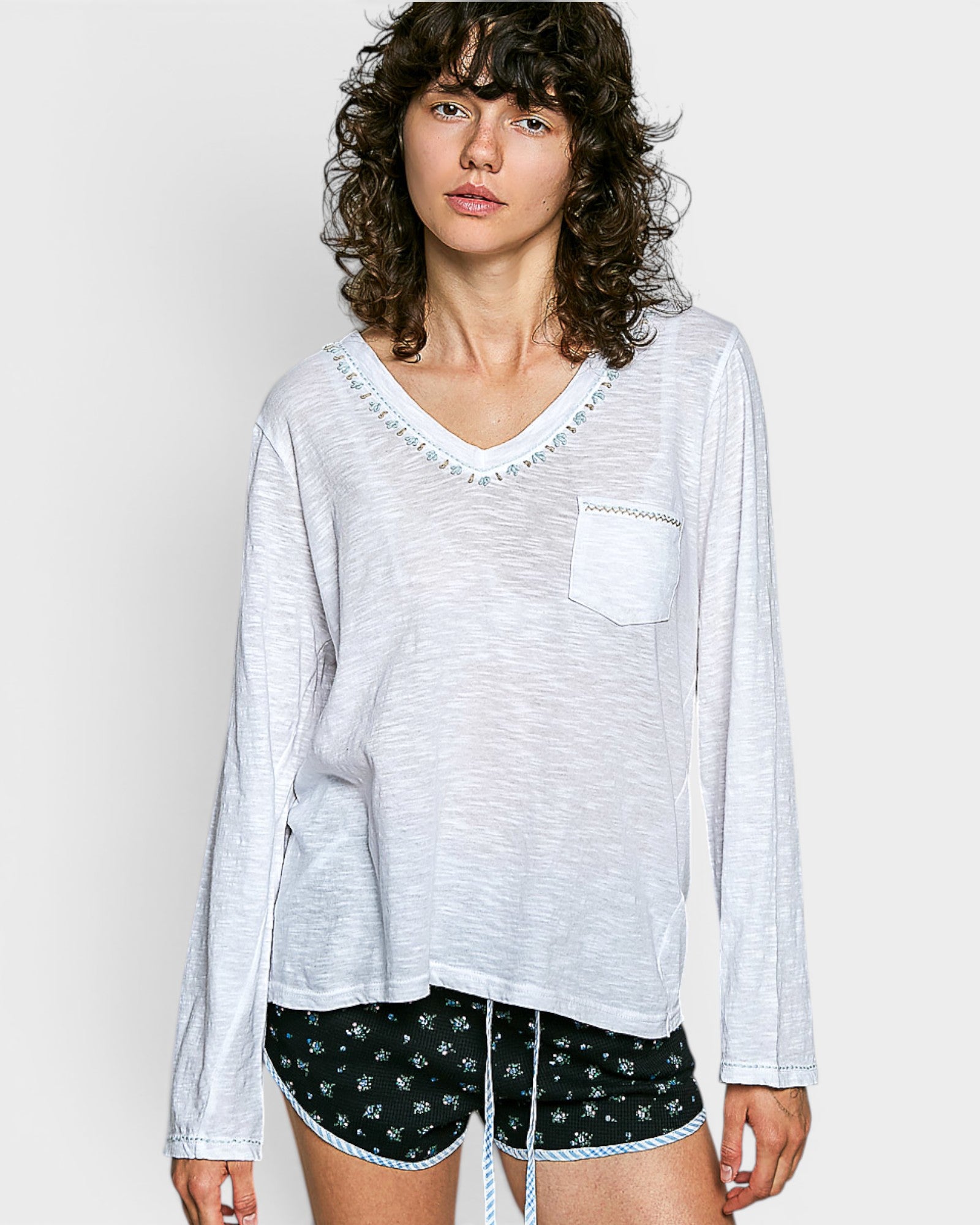 Woman wearing a white long-sleeve top with a pocket and black shorts with white patterns on a plain background