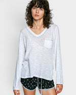 Woman wearing a white long-sleeve top with a pocket and black shorts with white patterns on a plain background