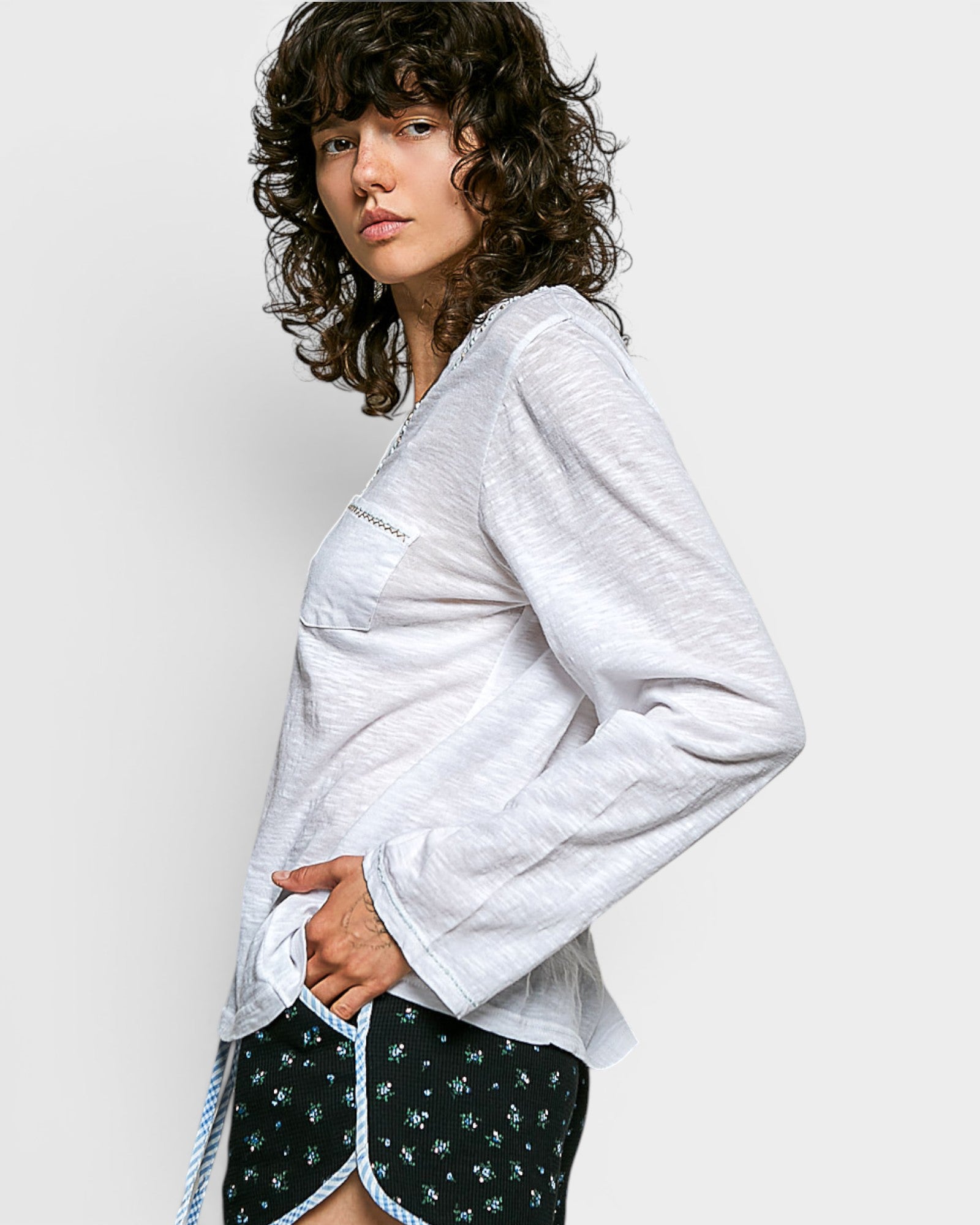 Woman wearing a white long-sleeve top with a pocket and black shorts with white patterns on a plain background