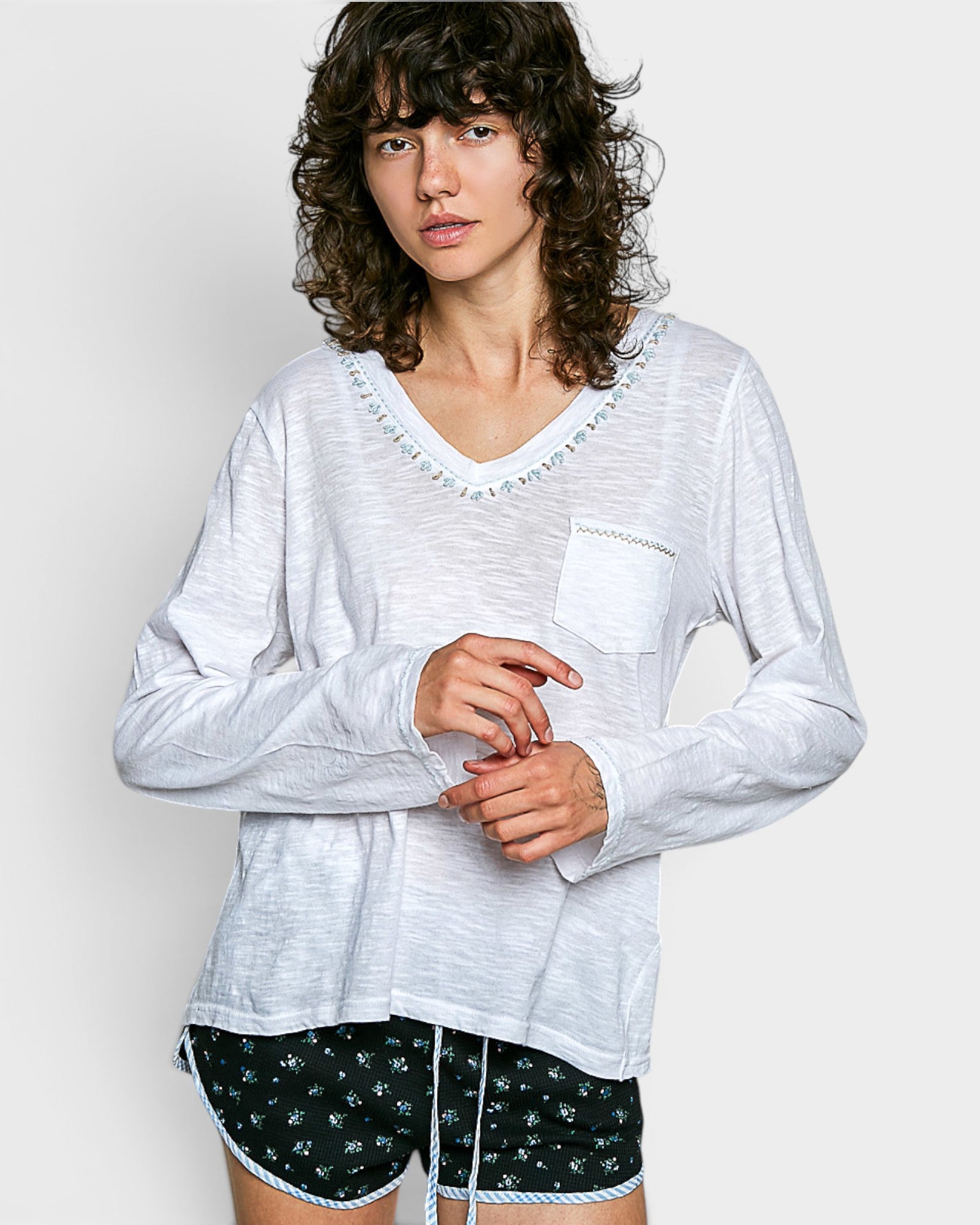 Woman wearing a white long-sleeve top with a pocket and black shorts with white patterns on a plain background