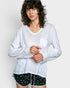 Woman wearing a white long-sleeve top with a pocket and black shorts with white patterns on a plain background
