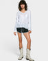 Woman wearing a white long-sleeve top, black shorts with white patterns, and white cowboy boots on a white background