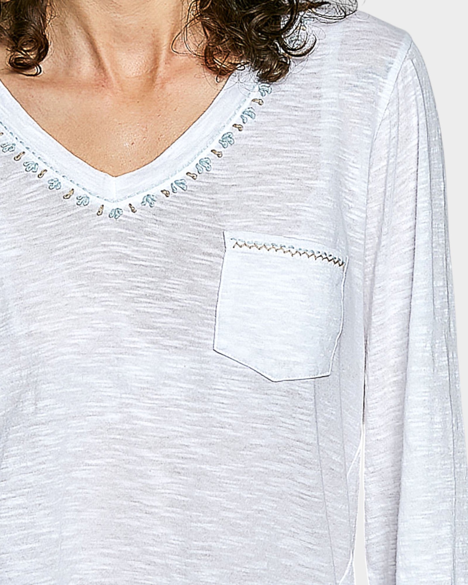 White long-sleeve top with decorative trim on neckline and pocket area.