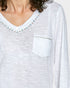 White long-sleeve top with decorative trim on neckline and pocket area.