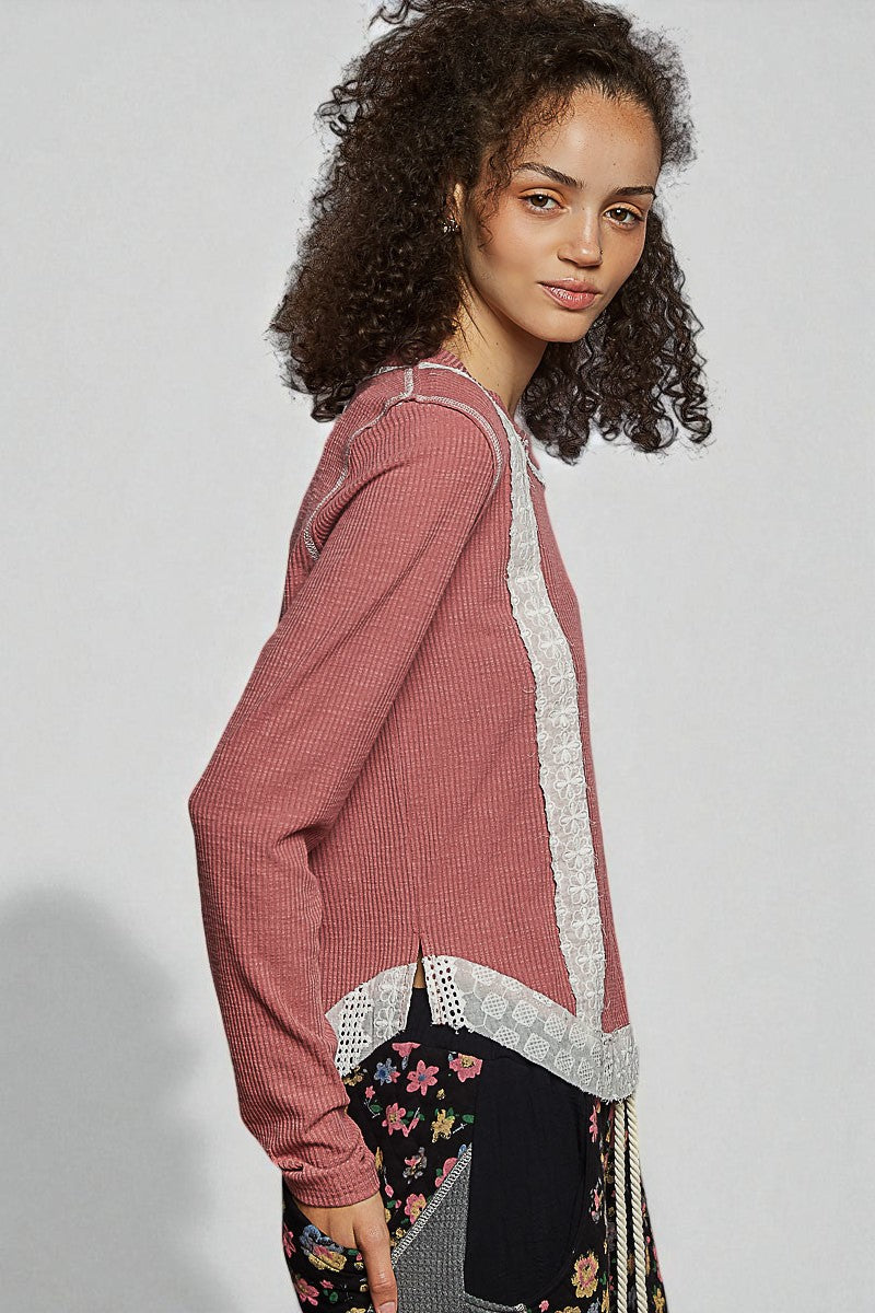 Woman wearing a pink cardigan with lace trim on a plain background