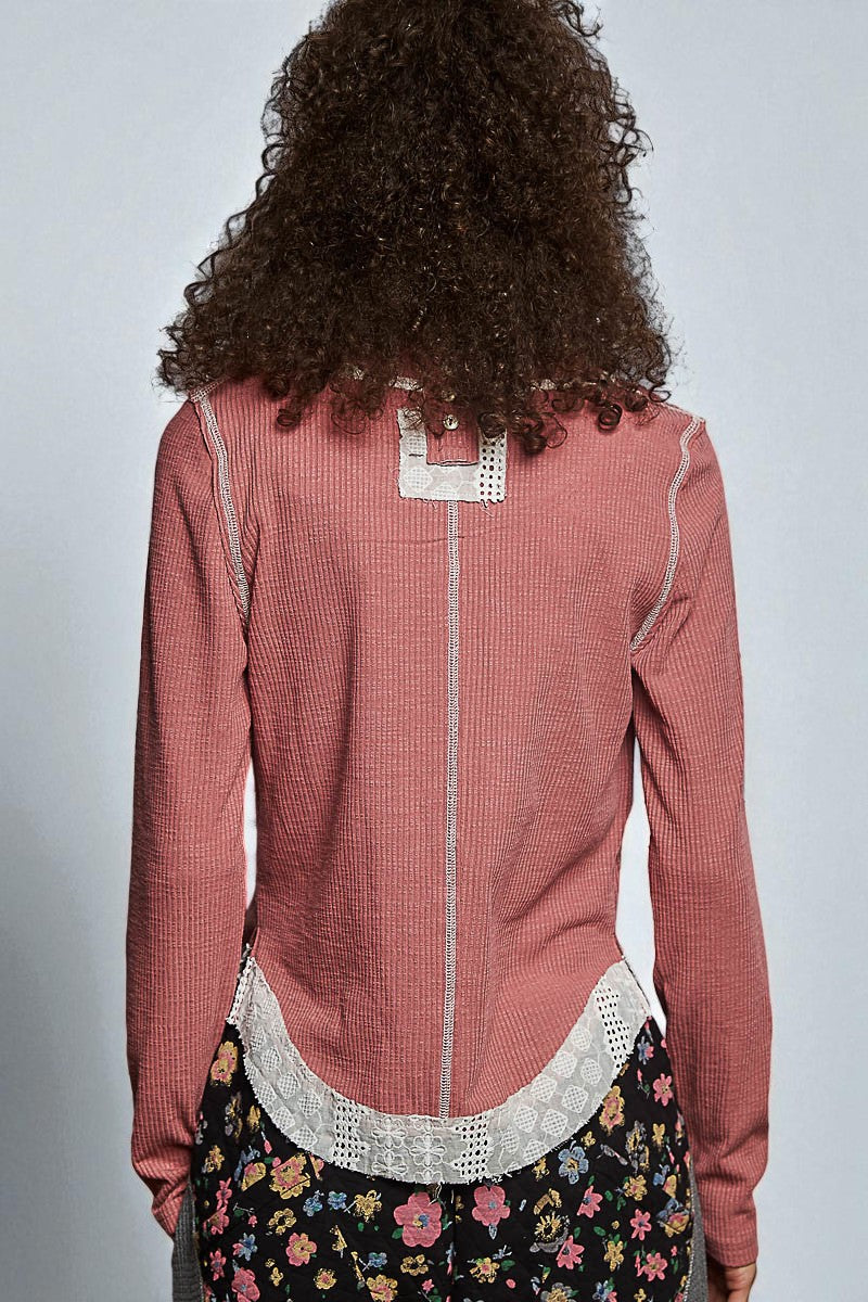 Person wearing a pink textured top with lace details and floral skirt on a plain background